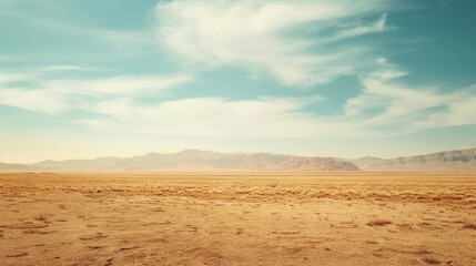 Fototapeta premium Vast desert landscape with a blue sky and white clouds, mountains in the distance.