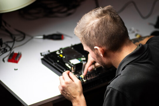 A man repairs a console, using a screwdriver to carefully open the device, focusing on its internal components and fan system.