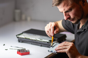 A man repairs a console, using a screwdriver to carefully open the device, focusing on its internal...