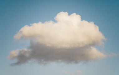 A single fluffy white cloud with soft edges floats peacefully in a clear blue sky. The cloud casts...