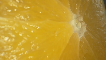 The macro photography of a sliced orange with vibrant orange color and visible in the juicy flesh of the citrus fruit. The flesh of the orange appears plump, hinting at its juiciness. Comestible.