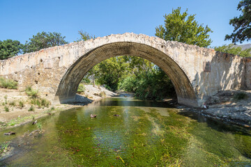 Old stone bridge remnant over small river with clear blue sky, side shot, symmetrical look, Greece, Crete island, wide angle lens