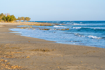 Empty, barren, sandy beach with small waves, clear blue sky, at sunset, telephoto