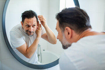 Man styling hair in front of bathroom mirror