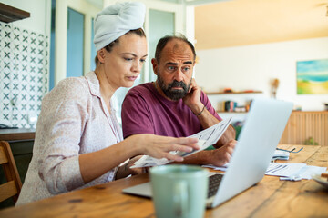 Fototapeta premium Couple reviewing bills together at home with laptop in kitchen