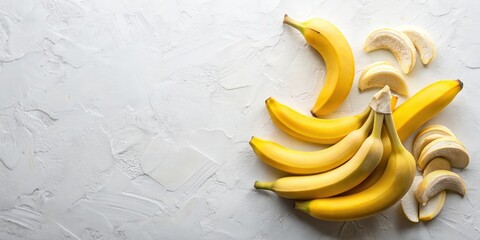A cluster of ripe yellow bananas with a few crescent-shaped slices on a white textured surface.