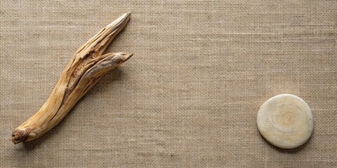 A rustic wooden twig and a smooth round wooden disc arranged on a textured burlap background