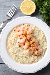 Delicious risotto with shrimps, cheese, lemon and parsley on grey wooden table, top view
