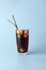 Tasty refreshing drink with straws in glass on light blue background