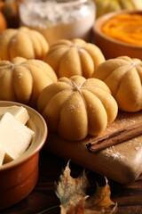 Raw pumpkin shaped buns and ingredients on wooden table, closeup