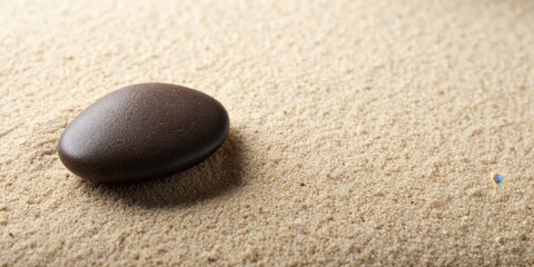 Obraz premium A solitary smooth brown stone rests on a bed of fine sand, casting a shadow that stretches towards the unseen horizon.