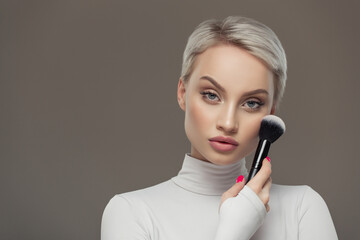 Portrait of a young girl with a makeup brush on a gray background.