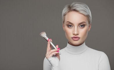 Obraz premium Portrait of a young girl with a makeup brush on a gray background.