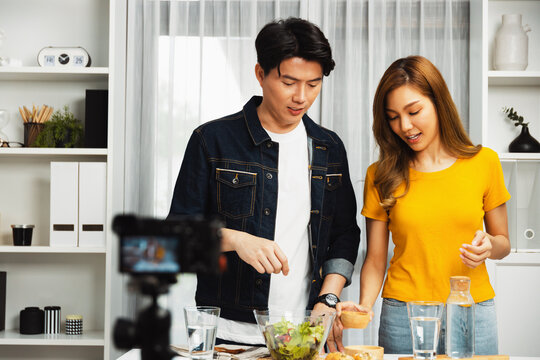 Cooking show on live streaming with two chef influencers teaching mixed salad with dressing for easy special recording on video camera. Ingredients placing bread bun wholegrain side dish. Infobahn.