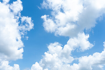 Fluffy cumulus clouds drift across the bright blue sky, casting soft shadows on the sunlit landscape