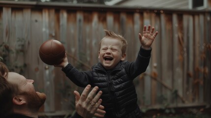 A Boy Laughing While Holding a Football with His Dad