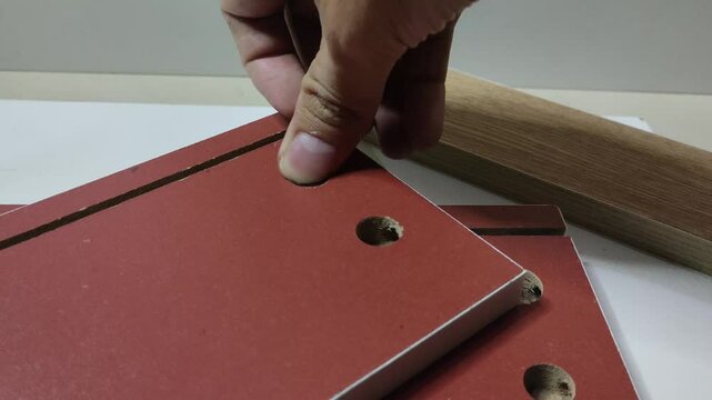 A man's hand places a minifix bolt into a hole provided on a brown wooden board.
