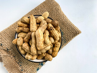 Unpeeled peanuts in a white bowl, on a white background. Unpeeled peanut isolated.