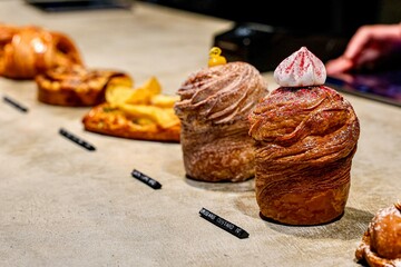 Display of artisanal pastries at a bakery. Close-up view of a bakery counter showcasing a selection of beautifully crafted pastries, including cruffins and other baked goods.