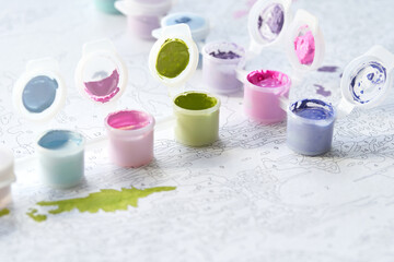 Colorful open paint pots on a numbered canvas for painting by numbers art project.