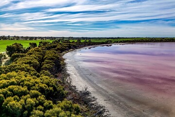 Aerial View of a Pink Salt Lake and Verdant Landscape. This serene aerial photograph captures a stunning contrast between a pink salt lake and lush green fields in the surrounding landscape. 