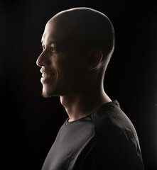 A smiling man in profile, illuminated against a dark background, showcasing his features.