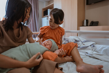 Sisters lovingly interact with their newborn sibling in a cozy home environment.