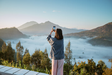 A woman is capturing stunning mountain views during the early morning hours at dawn