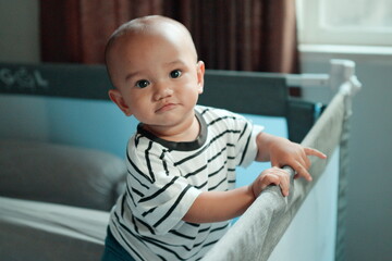 A playful and curious baby leans over the crib, showcasing their cuteness and innocence