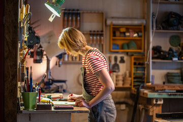 Female carpenter sketching furniture design and projects in woodworking workshop. Craftswoman...