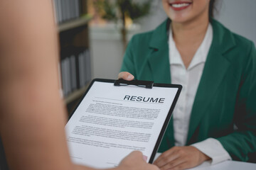 Smiling hr manager is holding a resume while interviewing a job applicant in her office