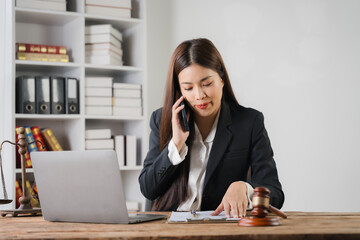 Focused Attorney: A professional woman in a black suit, engrossed in a phone conversation while reviewing documents at her desk. The gavel and bookshelves in the background suggest a legal setting.