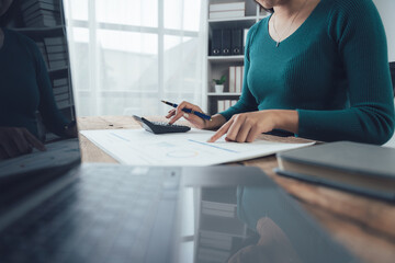 Focused Financial Planning: A woman meticulously reviews financial documents, using a calculator,...