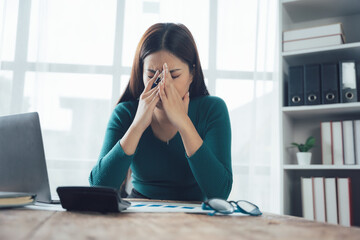 Obraz premium Overwhelmed by Workload: A woman sits at her desk, head in her hands, surrounded by documents and a calculator, conveying the stress and pressure of a demanding job. 