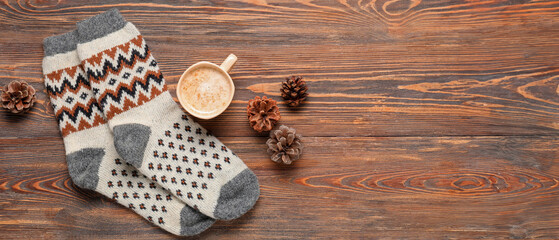 Warm socks with fir cones and cup of coffee on wooden background