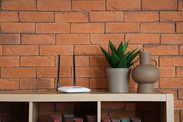 Modern wi-fi router with aloe and vase on shelf near brick wall