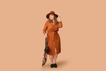 Beautiful young woman in stylish dress and hat with black bag on brown background