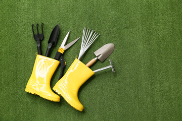 Set of gardening supplies in rubber boots on green grass. Top view