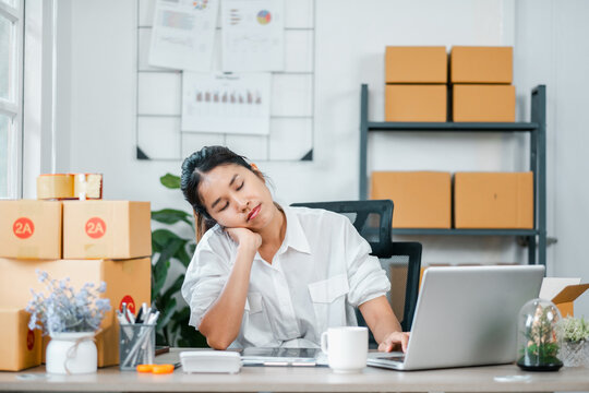 A young woman in a home office setting, taking a break from work. Surroundings include a laptop, shipping boxes, and office supplies. - Powered by Adobe