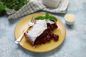 Plate with piece of tasty cherry strudel and napkin on blue grunge background