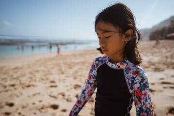 A cheerful child in colorful surf attire walks on the sandy beach, enjoying the sunny weather