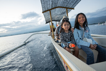 Two young girls are happily sitting together on a small boat that gently floats on the vast ocean, enjoying the beautiful scenery around them