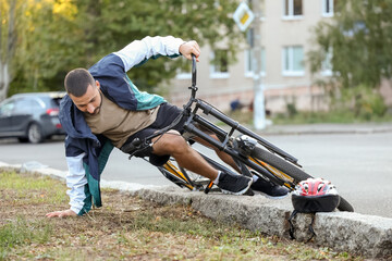 Obraz premium Young man falling off his bike onto grass outdoors
