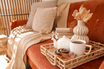 Tray with cup of hot tea, tasty poppy buns and teapot on sofa at home, closeup