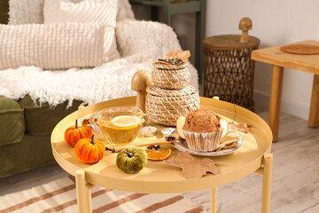 Cup of tea, muffin, burning candles and autumn decor on coffee table in room
