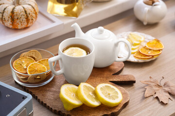 Teapots, cup of green tea, lemon and autumn decor on table in room. Closeup