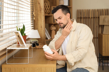 Handsome man with thyroid gland problem and pill bottle sitting at home