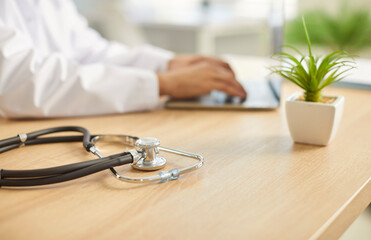 Close up of male doctor sitting at the desk on workplace in medical clinic with stethoscope in...