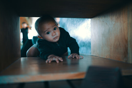 A small baby crawls playfully under furniture, showcasing curiosity and exploration