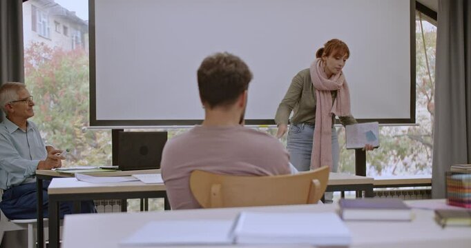 A confident young female college student gives a presentation to a small group in the classroom, articulating her ideas clearly and engaging her audience with her well-prepared material.